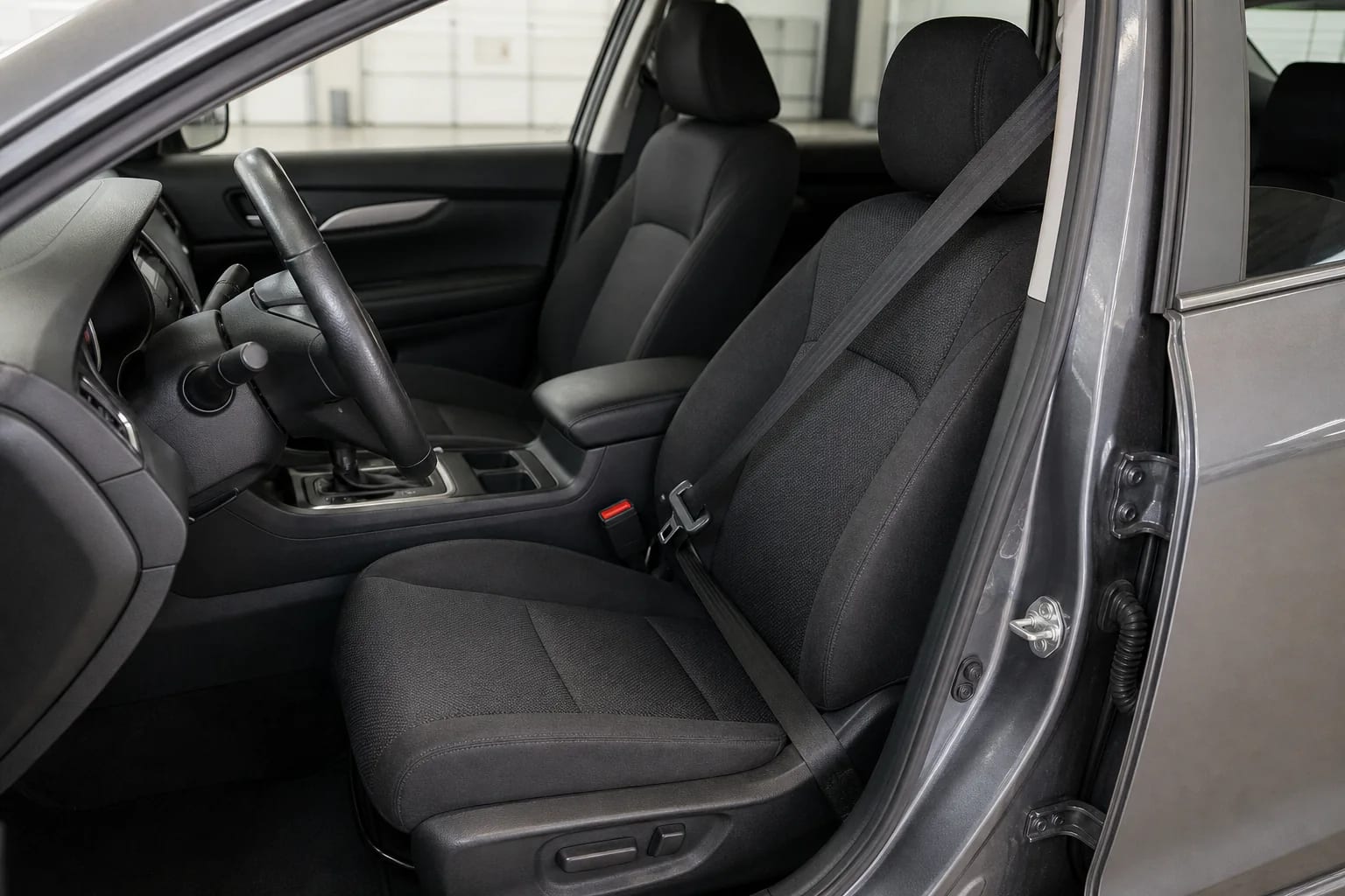 Intact driver seat belt, buckle, seat, and steering wheel inside an unbranded vehicle in a clean inspection bay