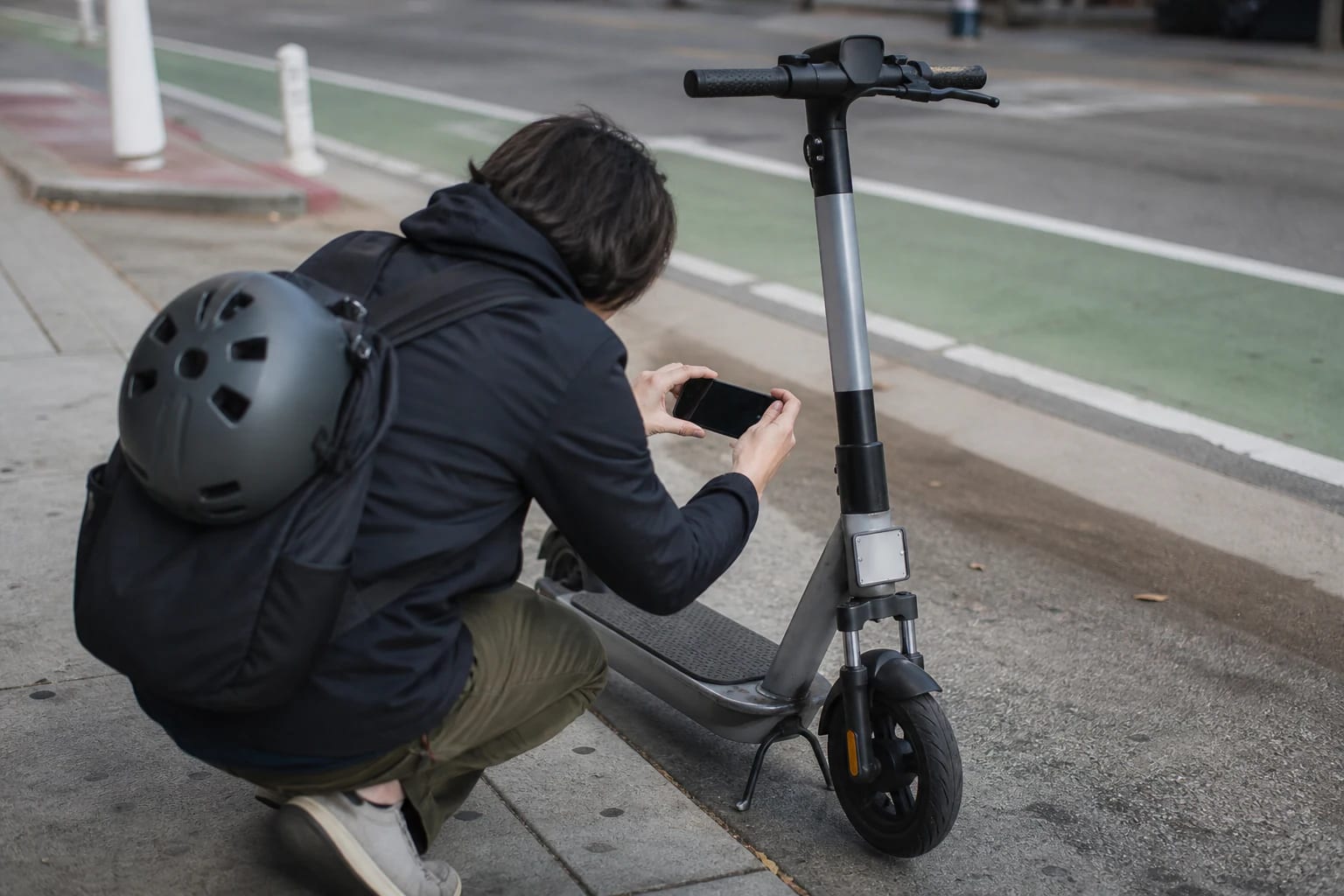 Person photographing an identification plate on a shared e-scooter beside a bike lane
